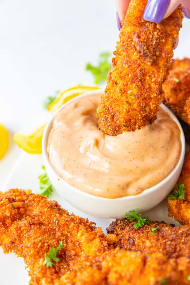 a chicken finger dipped in sauce in a white bowl.