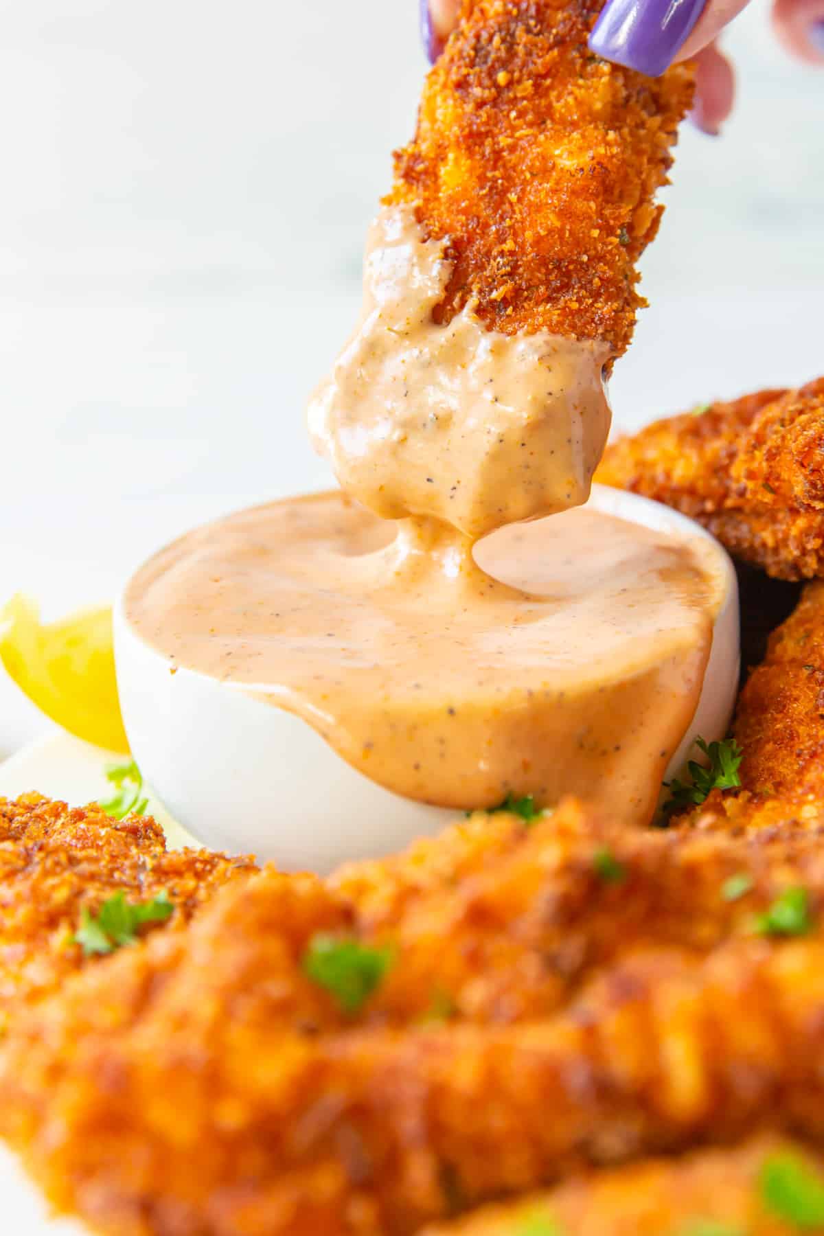 a chicken finger dipped in sauce in white bowl.