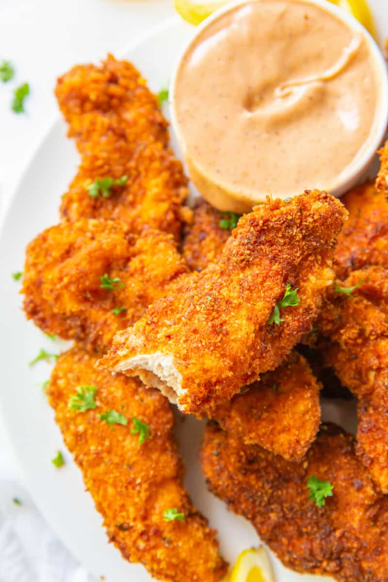 a plate of chicken fingers and sauce with a bite taken out of one.