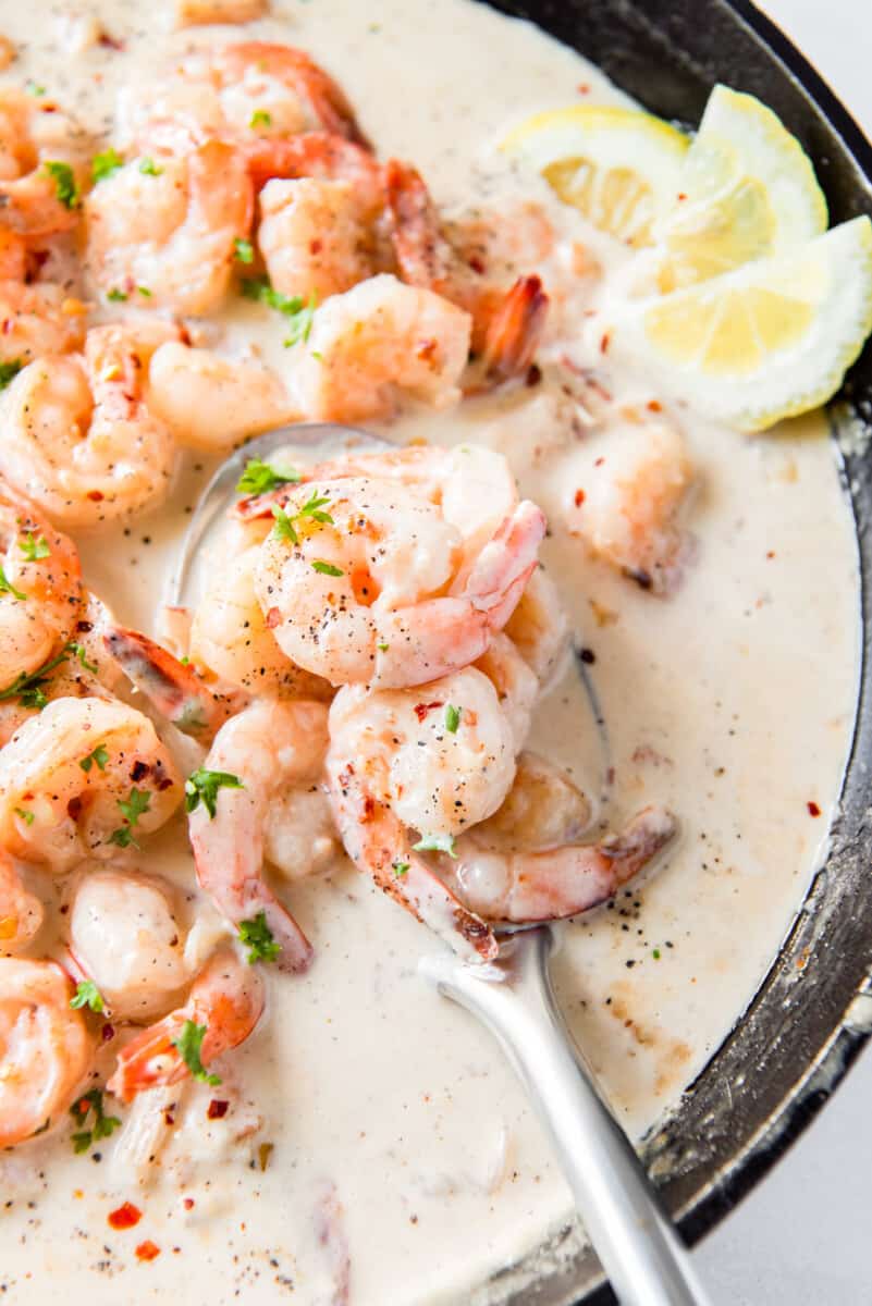 close up of creamy parmesan shrimp in a skillet with a spoon.