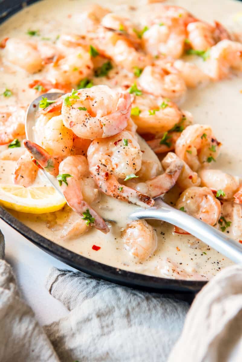 close up of creamy parmesan shrimp in a skillet with a spoon.