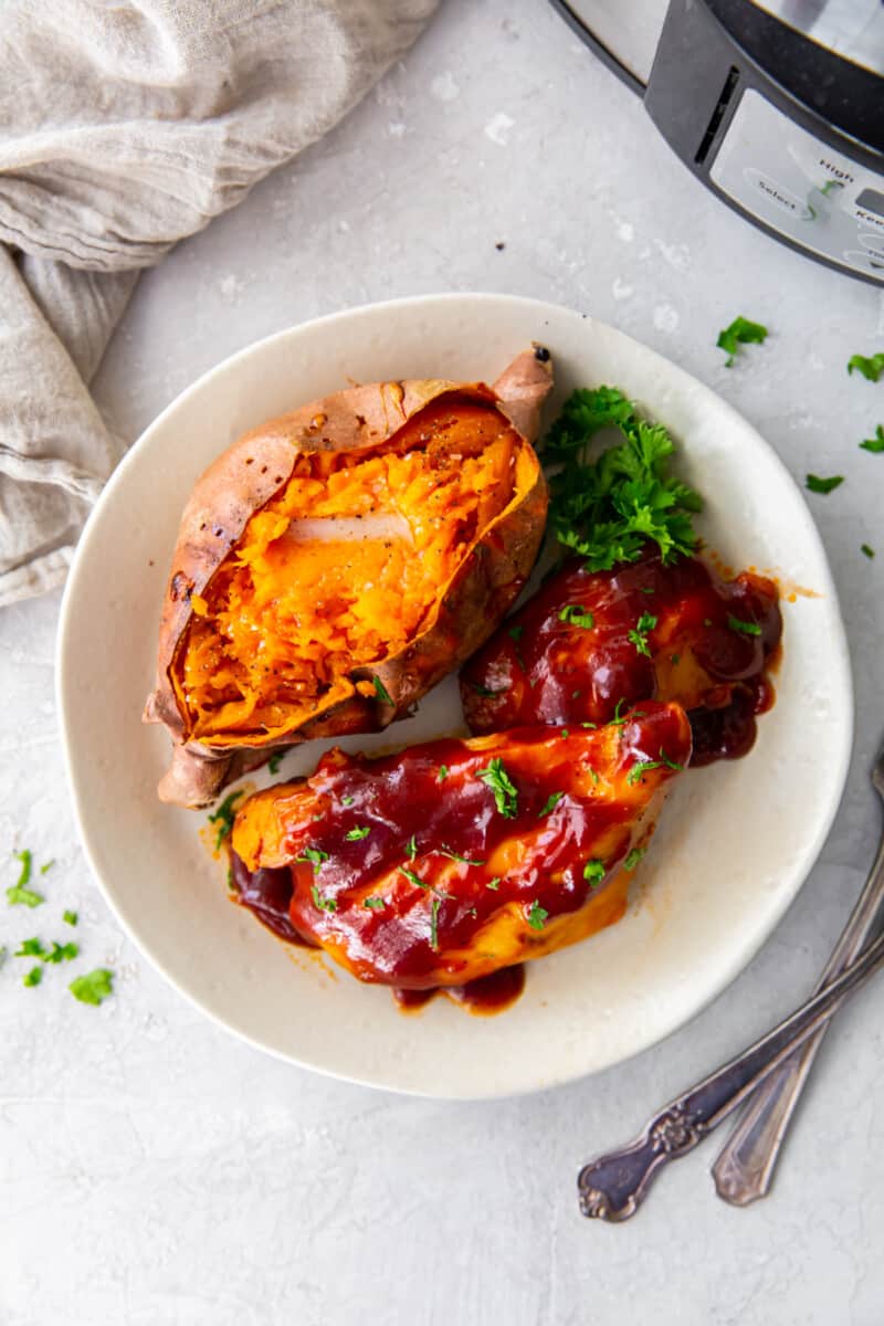 crockpot bbq chicken with sweet potato and parsley on a white plate.