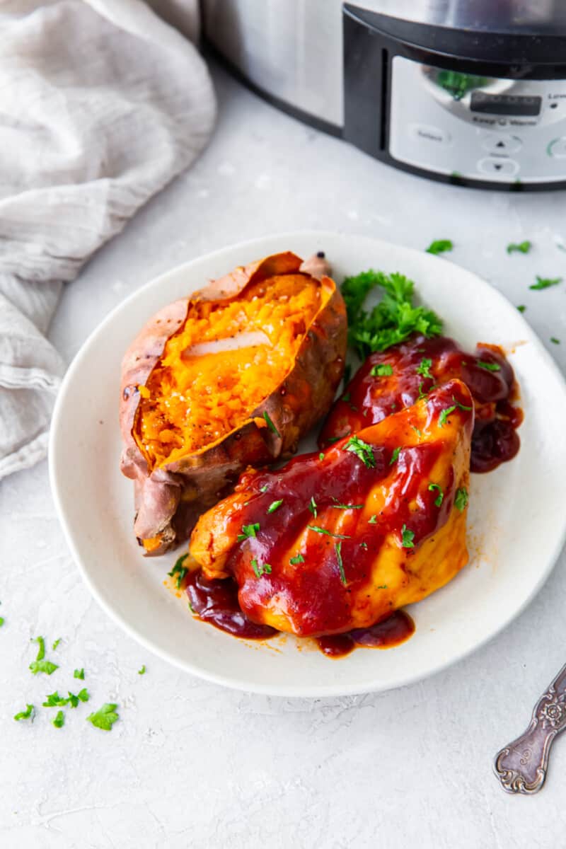 crockpot bbq chicken with sweet potato and parsley on a white plate.