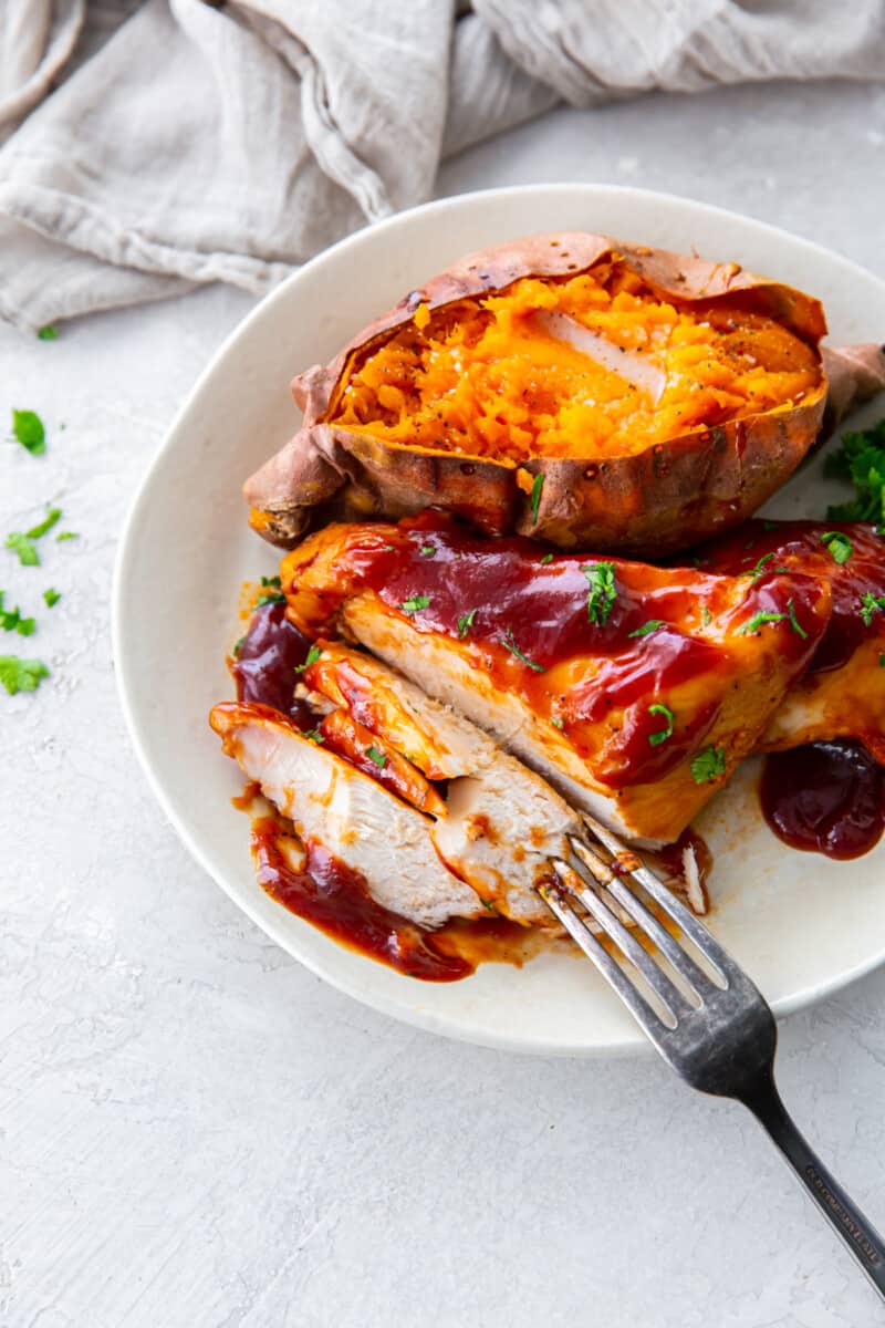 forkful of crockpot bbq chicken on a white plate with sweet potato.