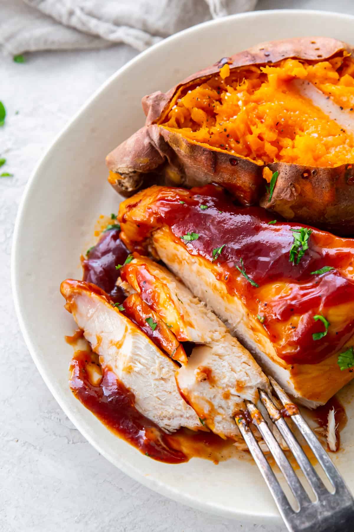 forkful of crockpot bbq chicken on a white plate with sweet potato.