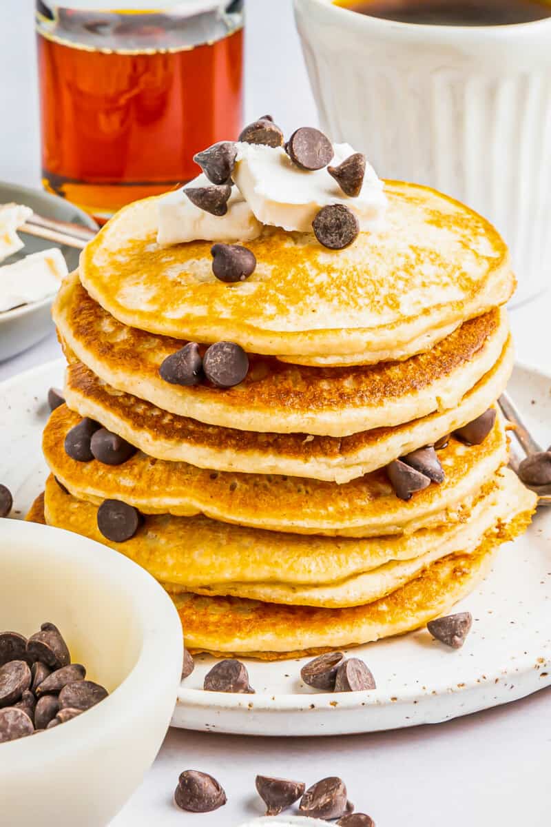 a tall stack of gluten free pancakes on a white plate with chocolate chips and butter.