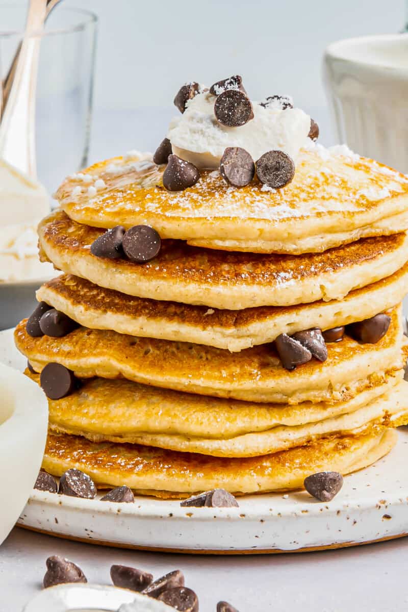 a tall stack of gluten free pancakes on a white plate with chocolate chips and butter.