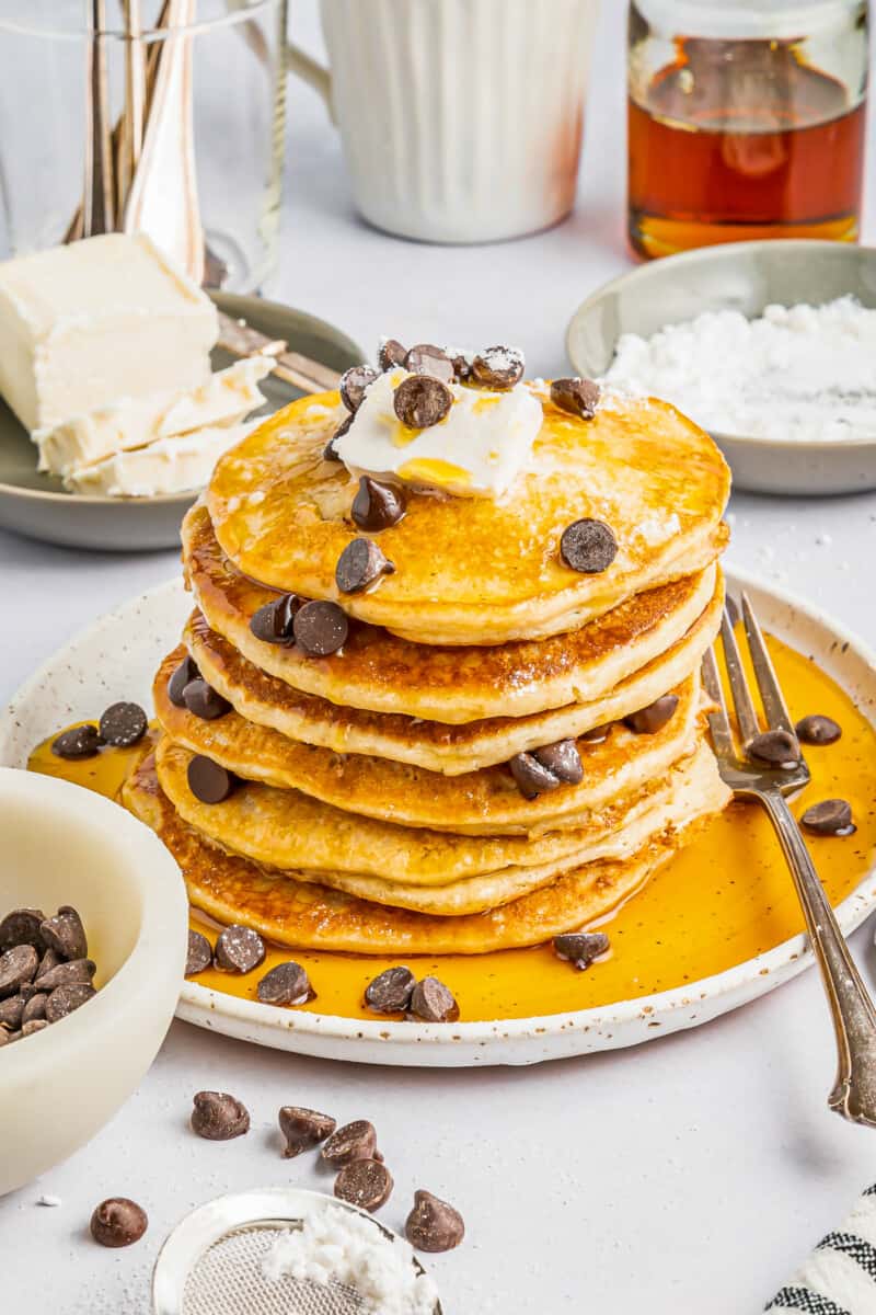 a tall stack of gluten free pancakes on a white plate with chocolate chips butter and a fork.