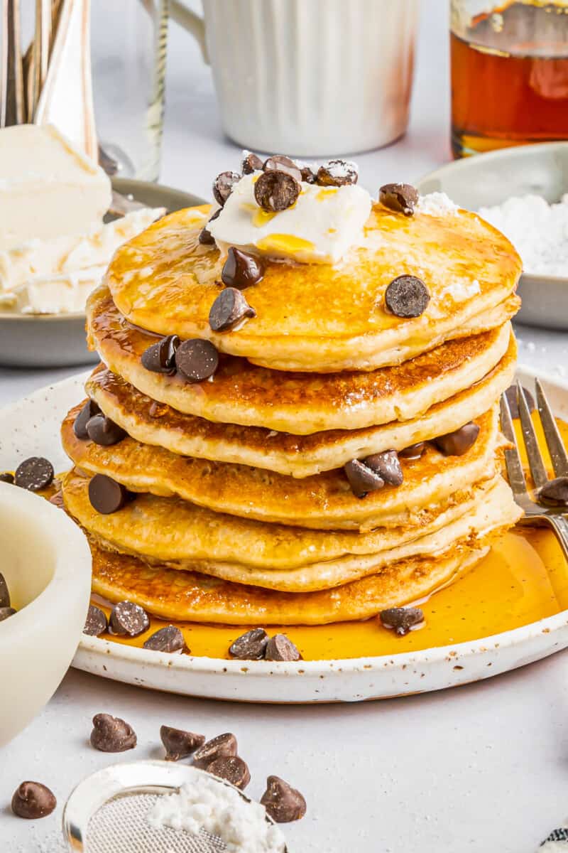 a tall stack of gluten free pancakes on a white plate with chocolate chips butter and a fork.