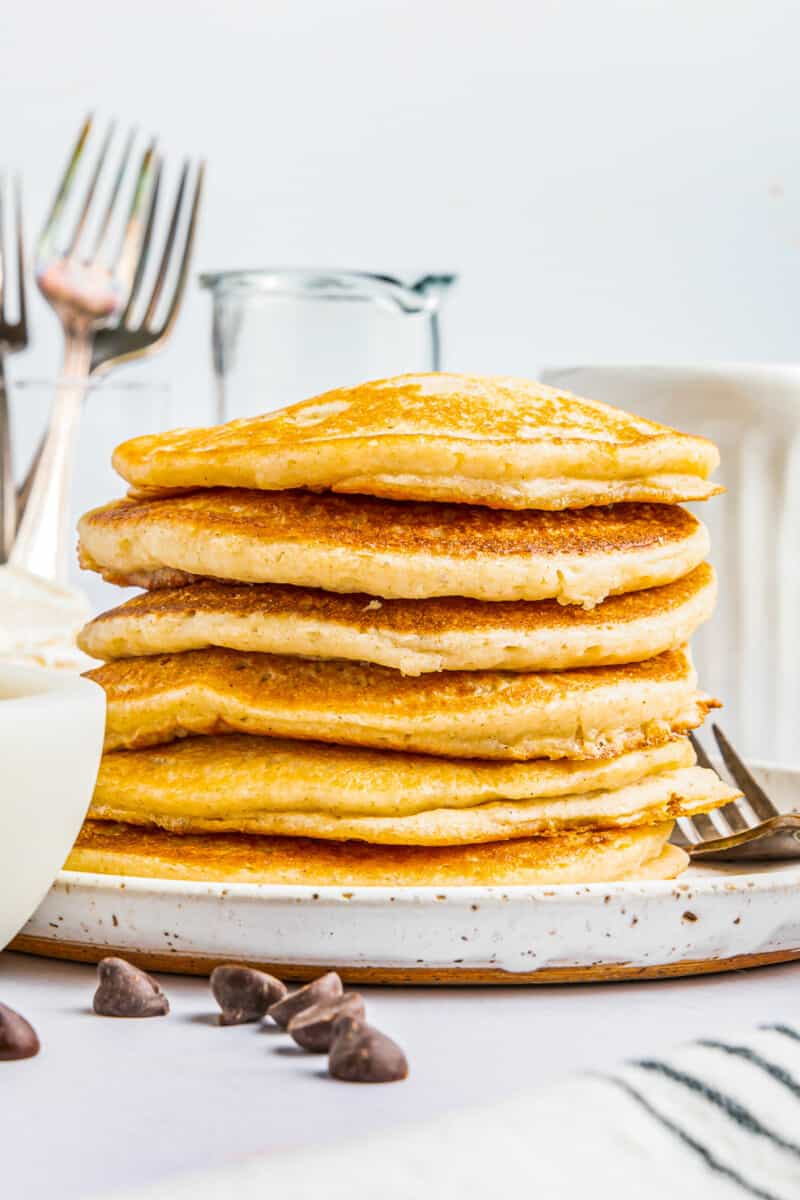 a tall stack of gluten free pancakes on a white plate with a fork.