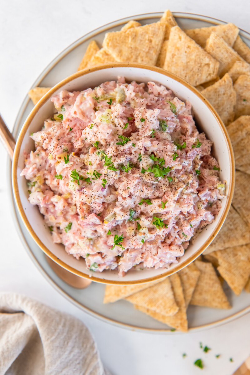 ham salad in a white bowl on a white plate with triscuits.