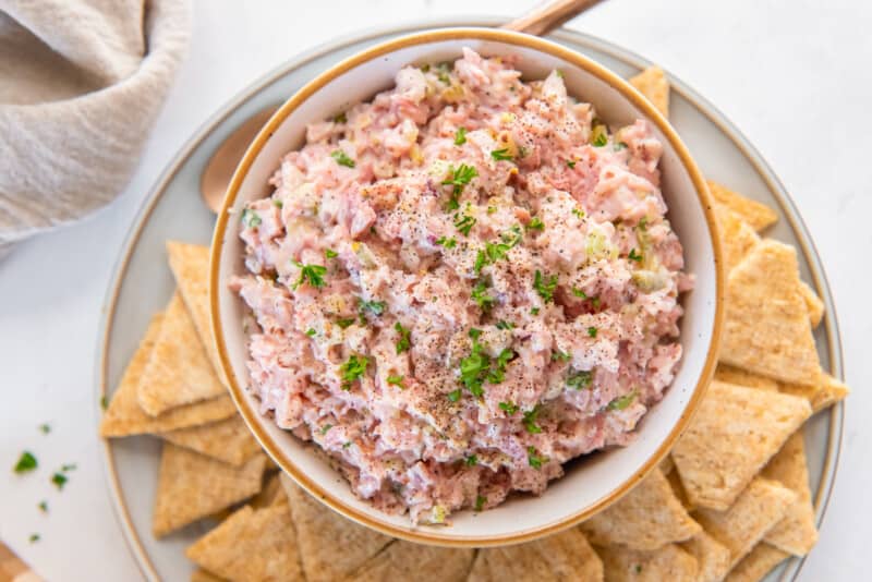 ham salad in a white bowl on a white plate with triscuits.