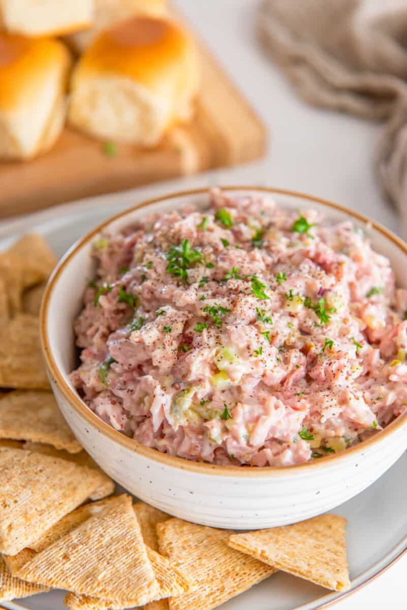 ham salad in a white bowl on a white plate with triscuits.