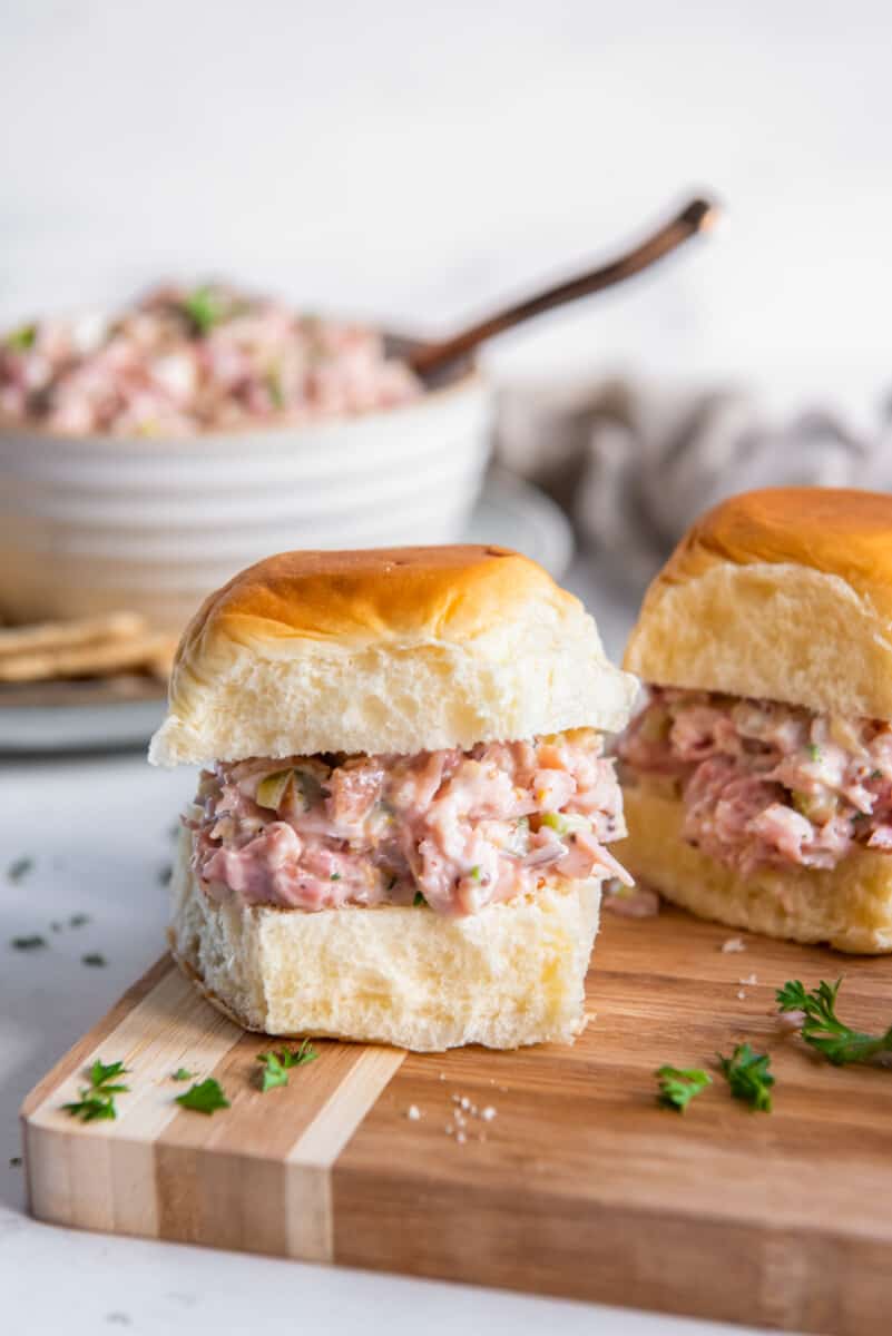 ham salad on slider rolls on a wooden cutting board.