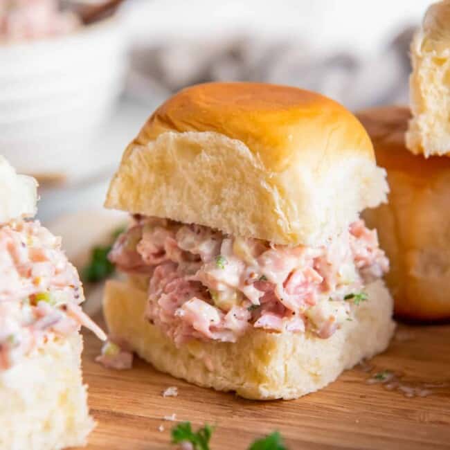 ham salad on slider rolls on a wooden cutting board.