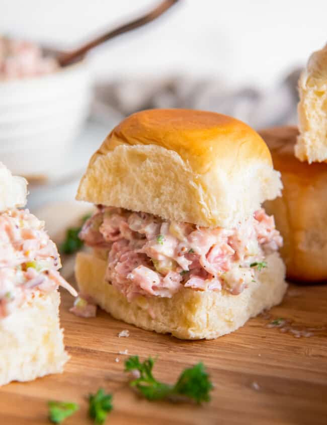 ham salad on slider rolls on a wooden cutting board.