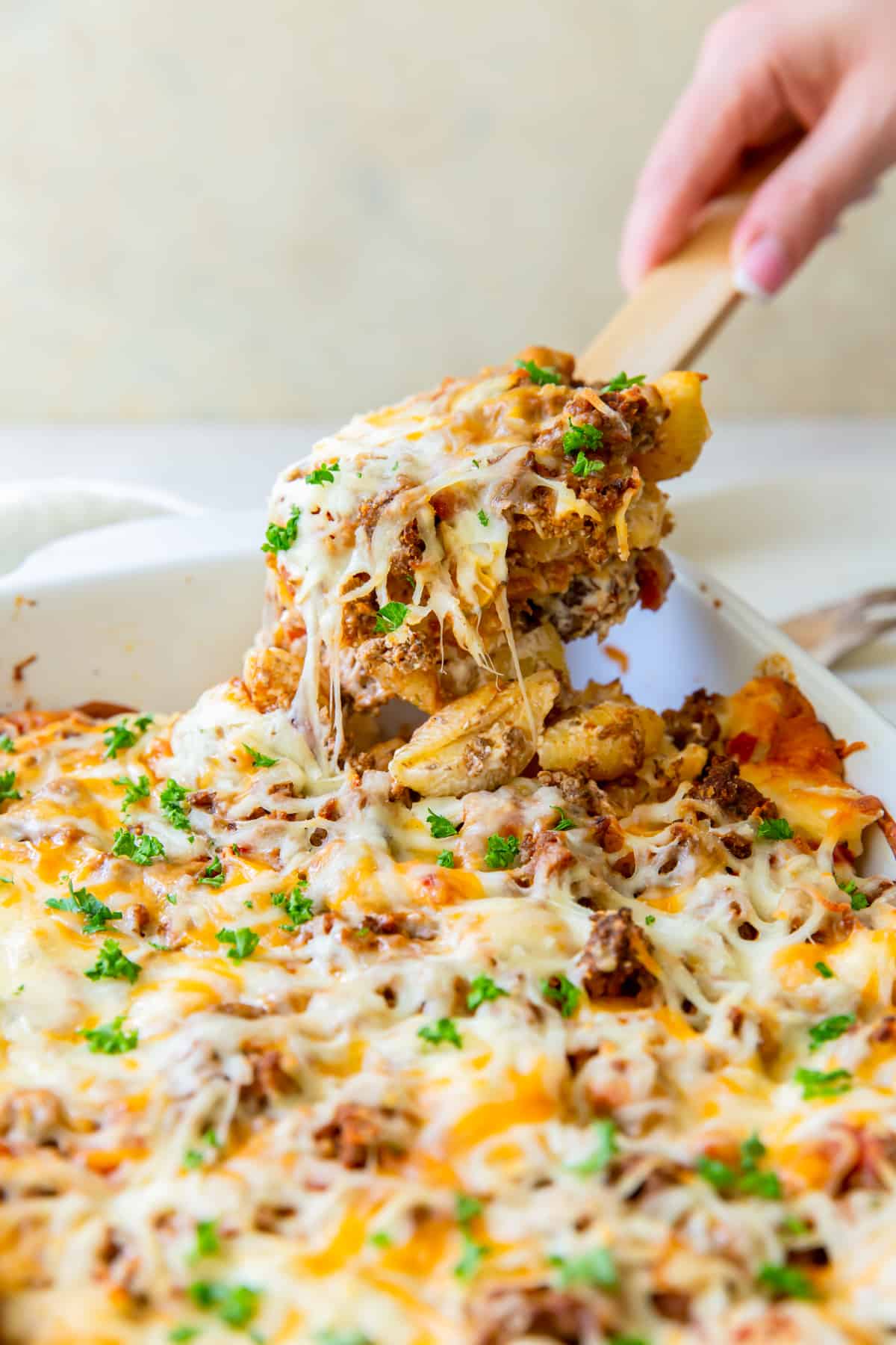 hand scooping out a serving of hamburger casserole with a wood spoon