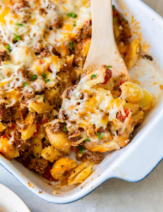 hamburger casserole in a white baking dish with a wood serving spoon
