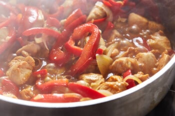 chicken and peppers in a skillet with sauce.