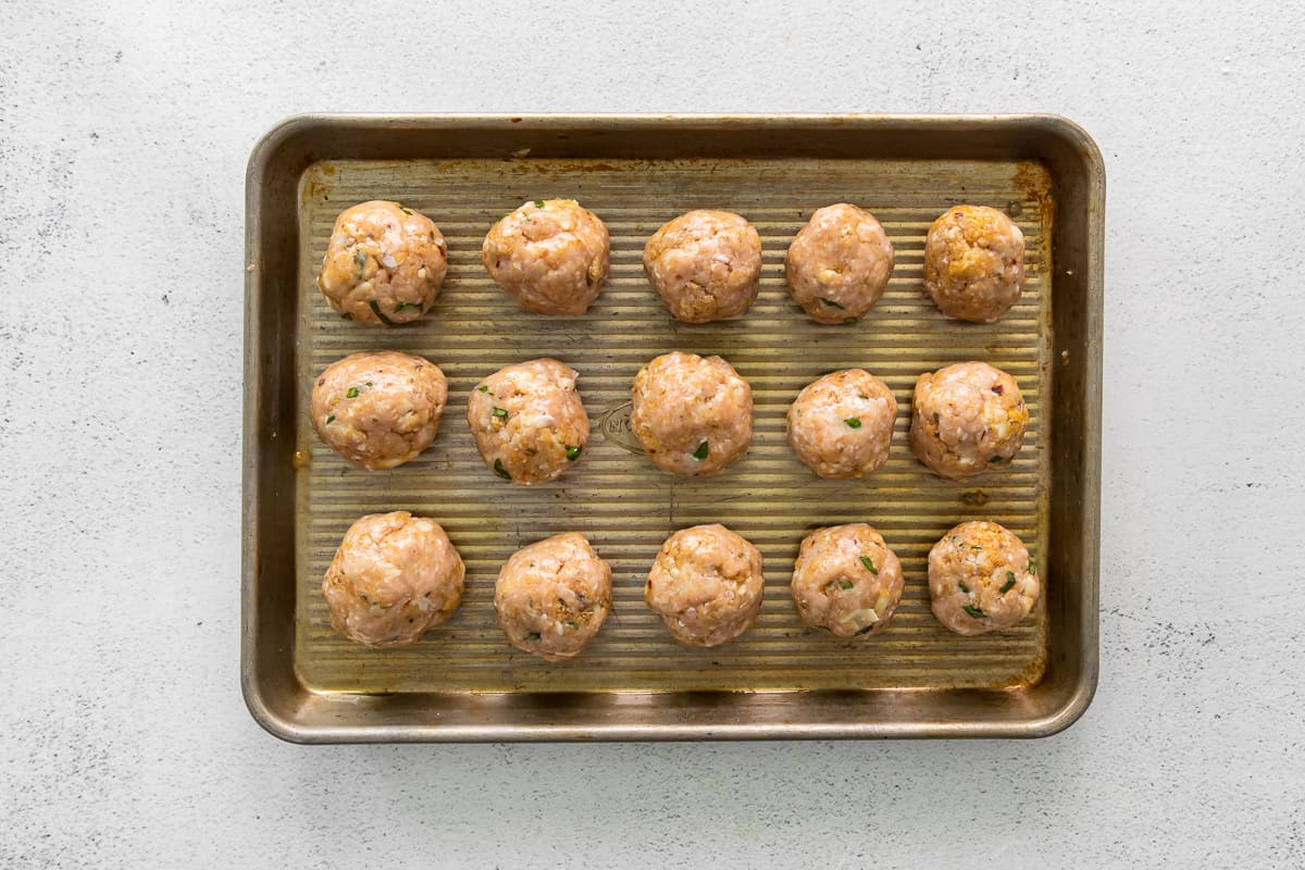 15 rolled unbaked chicken Parmesan meatballs on a sheet tray.