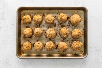 15 rolled baked chicken parmesan meatballs on a sheet tray.