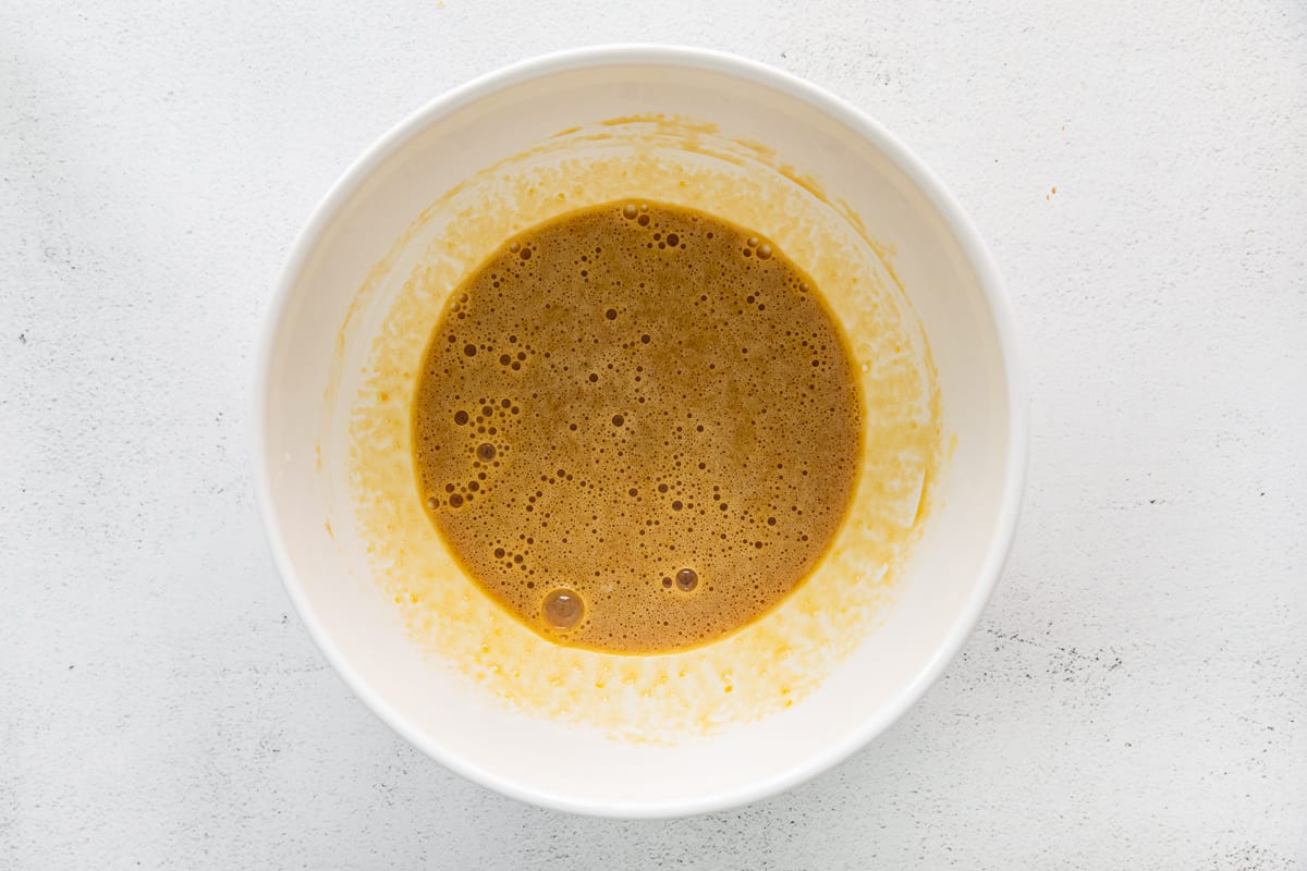 overhead view of eggs and brown sugar whisked together in a white bowl.