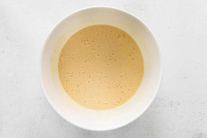 overhead view of mixed wet ingredients for cinnamon roll bread in a white bowl.