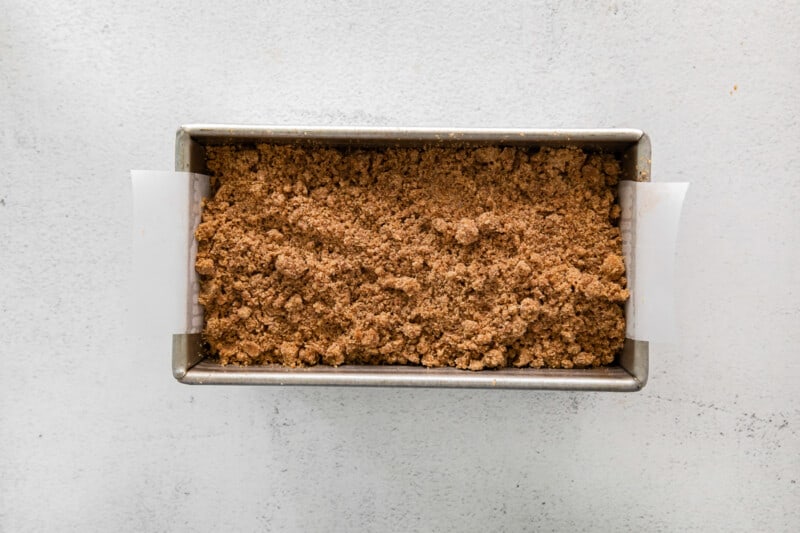 overhead view of streusel topped cinnamon roll bread in a parchment lined loaf pan.