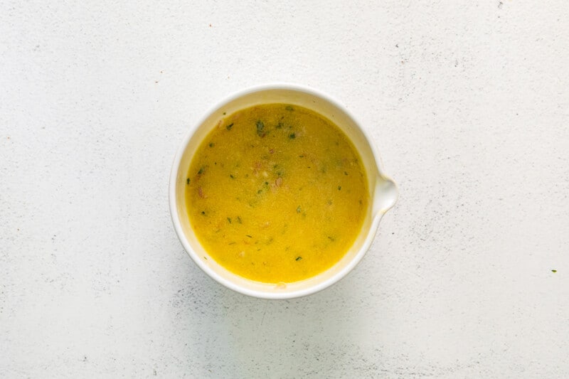 overhead view of lemon vinaigrette for mediterranean orzo salad in a white bowl.