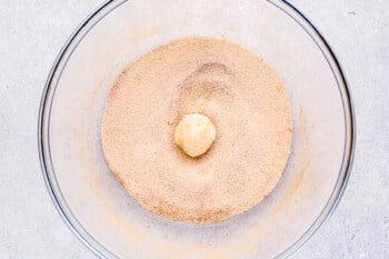 a ball of biscuit dough dipped in cinnamon sugar in a glass bowl.