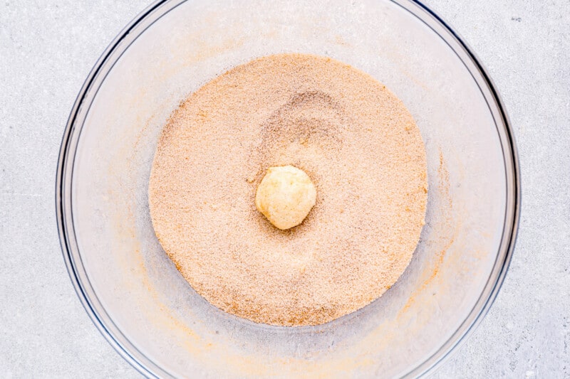 a ball of biscuit dough dipped in cinnamon sugar in a glass bowl.