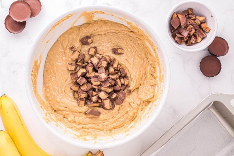 peanut butter cups added to reeses peanut butter cup banana bread batter in a white bowl.