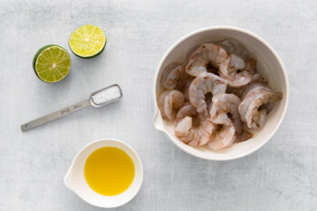 raw shrimp in a white bowl with limes.