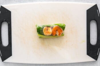 1 shrimp summer roll on a white cutting board.