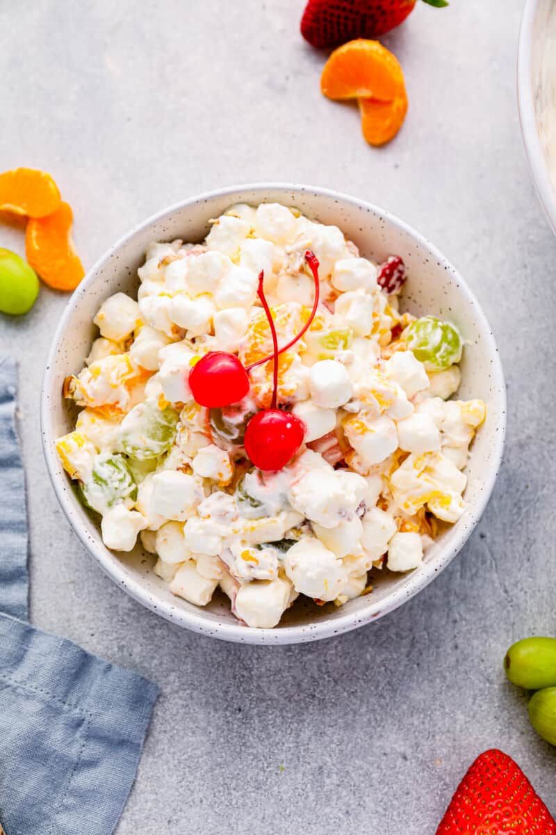 marshmallow salad in a white bowl with 2 maraschino cherries.