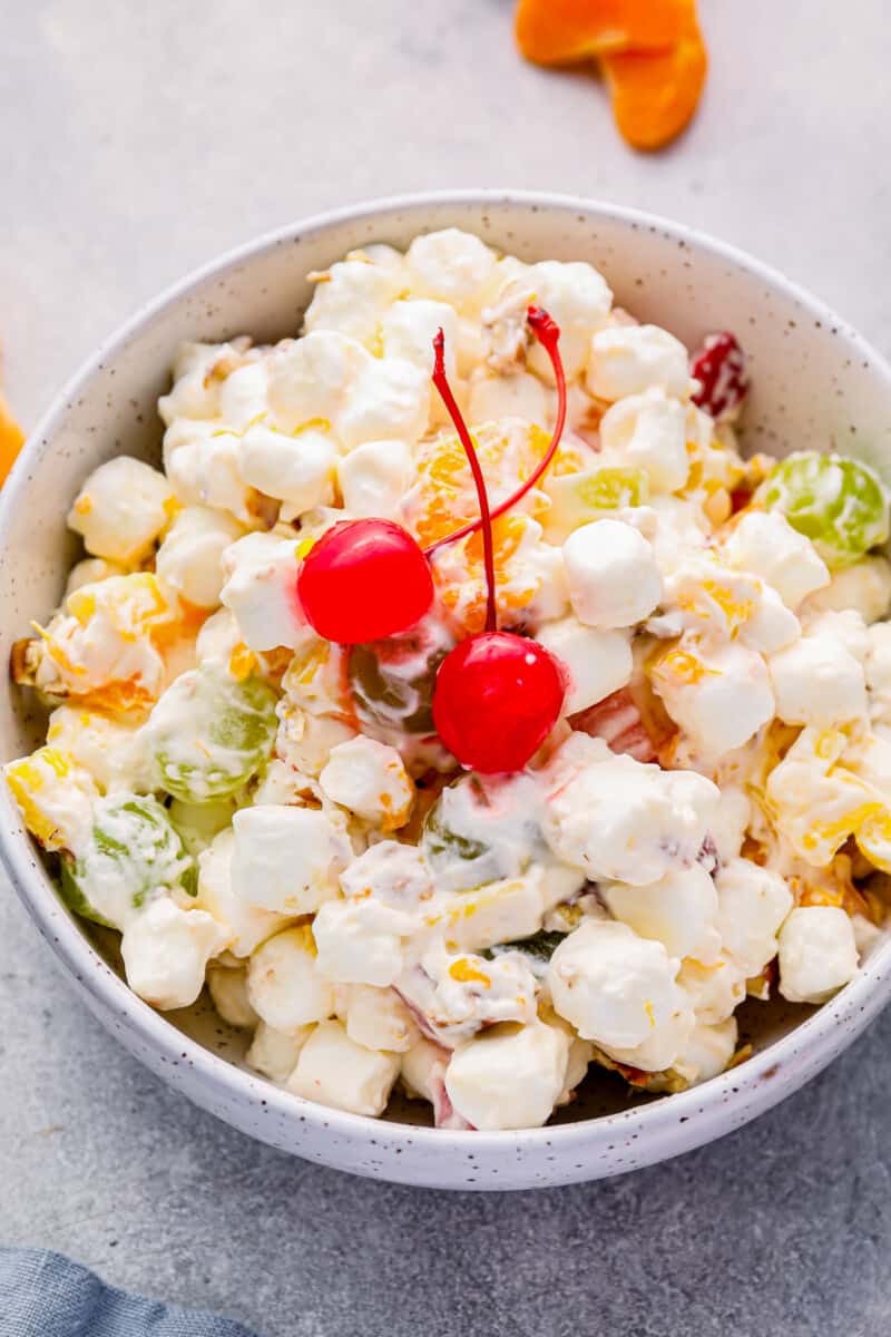 marshmallow salad in a white bowl with 2 maraschino cherries.