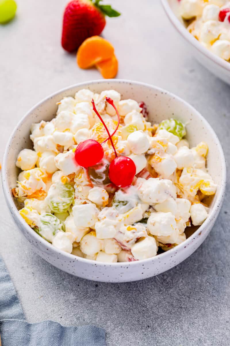 marshmallow salad in a white bowl with 2 maraschino cherries.