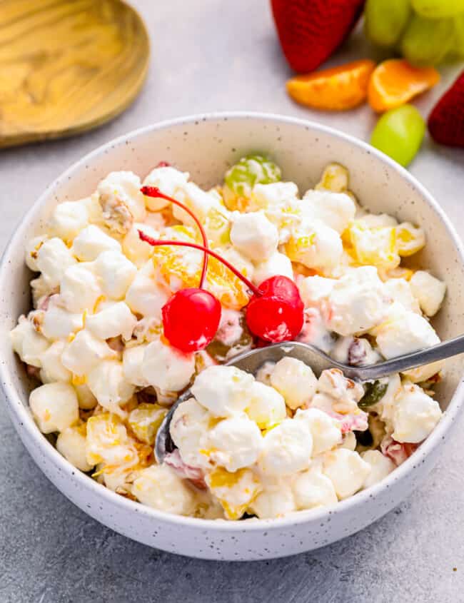 marshmallow salad in a white bowl with 2 maraschino cherries and a spoon.