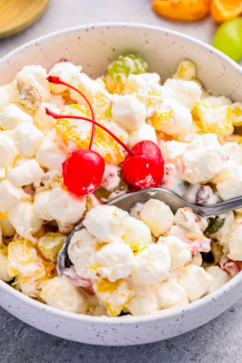 marshmallow salad in a white bowl with 2 maraschino cherries and a spoon.