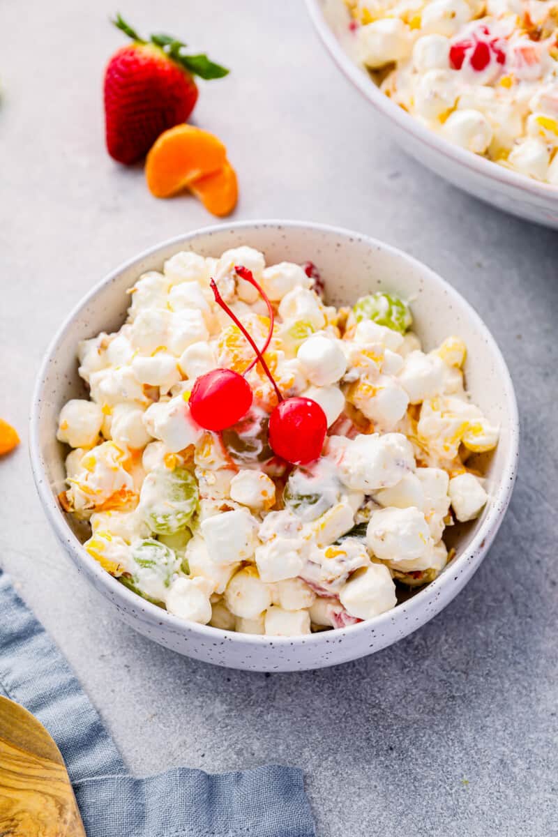 marshmallow salad in a white bowl with 2 maraschino cherries.