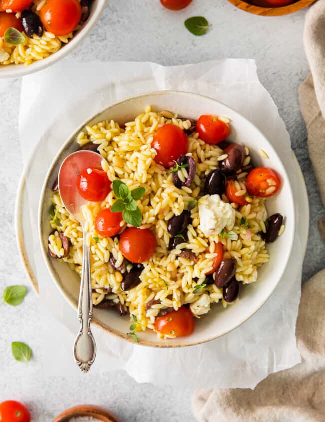 mediterranean orzo salad in a white bowl with a spoon.