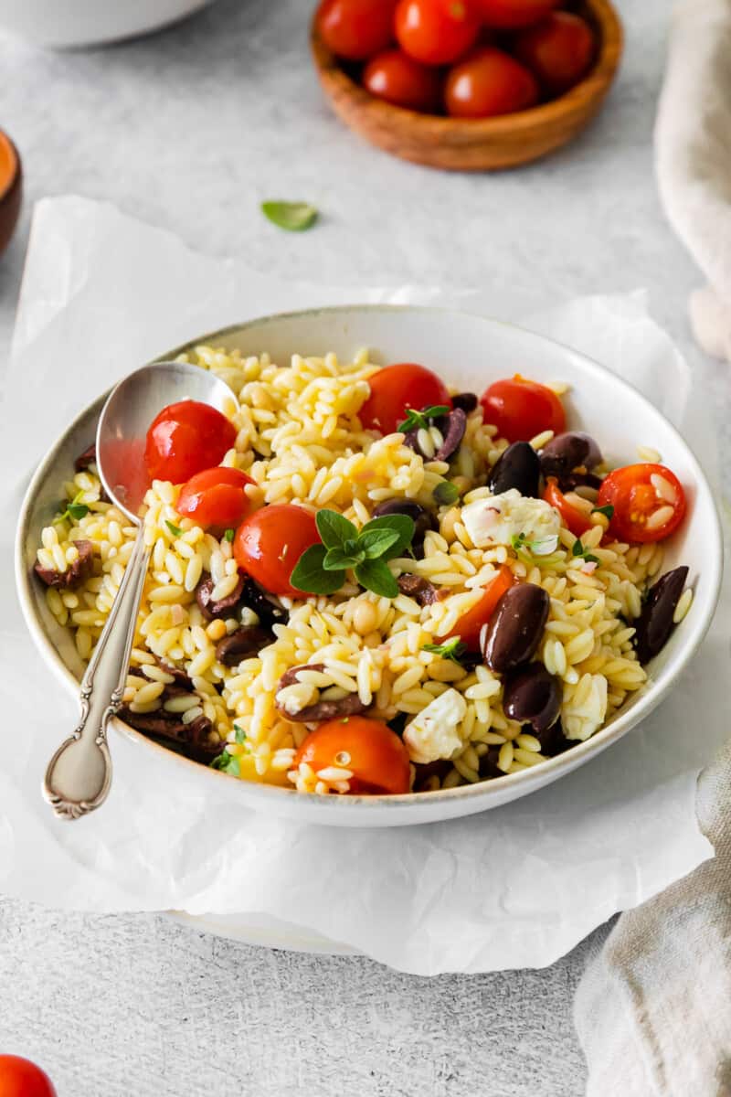 mediterranean orzo salad in a white bowl with a spoon.