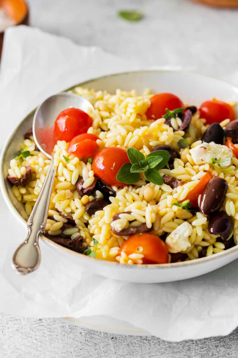 mediterranean orzo salad in a white bowl with a spoon.