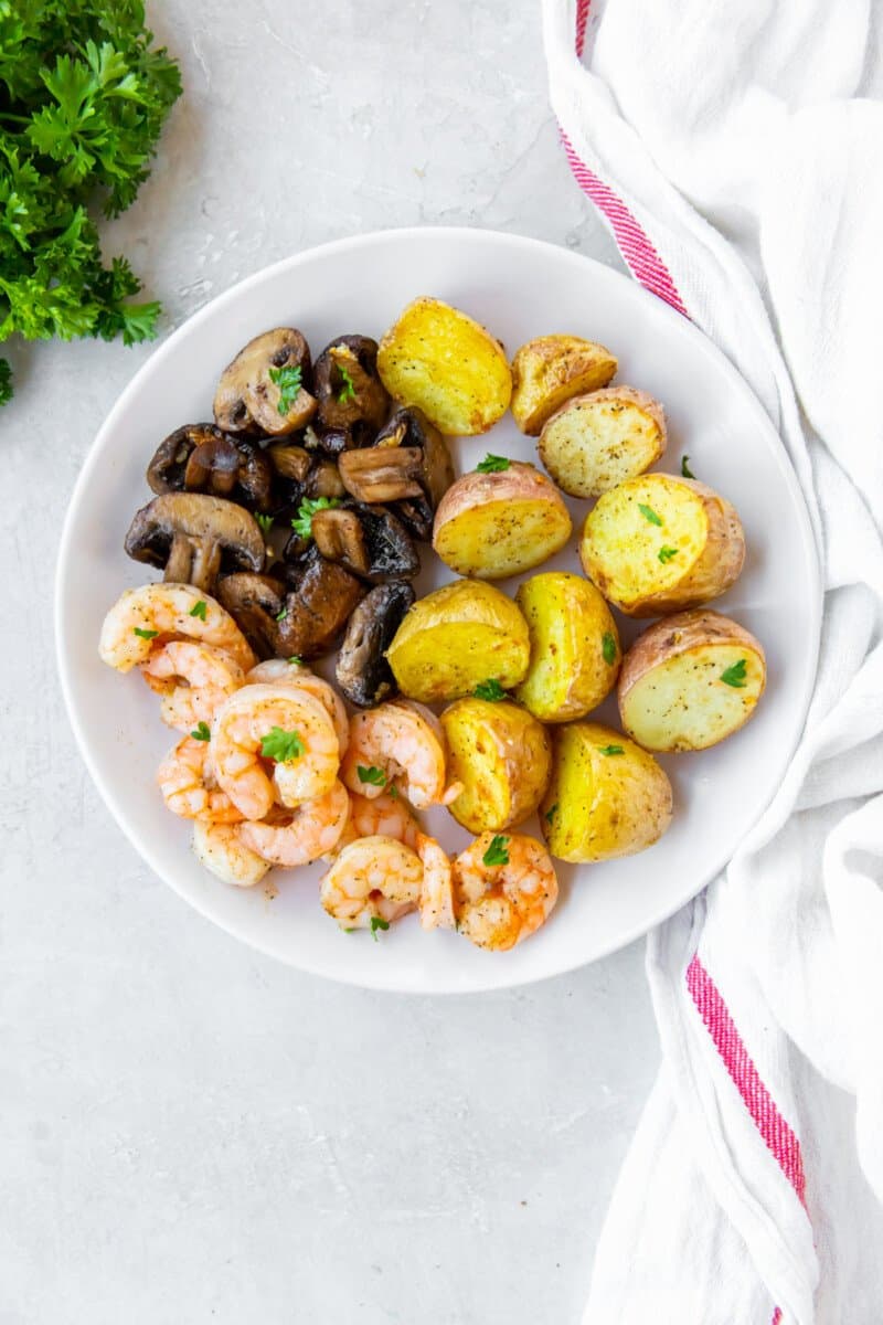 air fryer garlic shrimp on a white plate with potatoes and mushrooms.