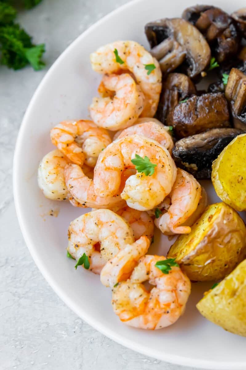 close up of air fryer garlic shrimp on a white plate with potatoes and mushrooms.