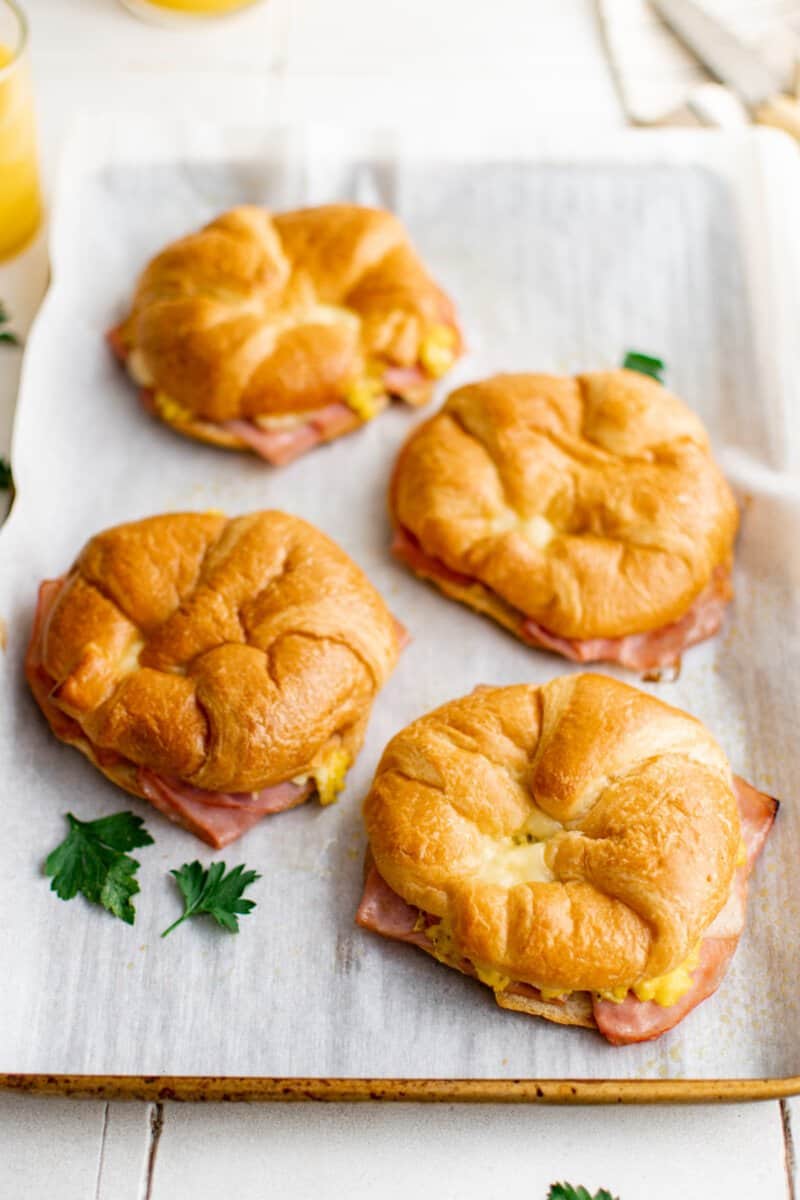 4 croissant breakfast sandwiches on a baking sheet.