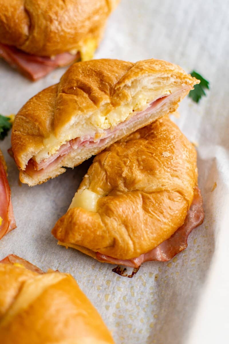 stacked croissant breakfast sandwich halves on a baking sheet.