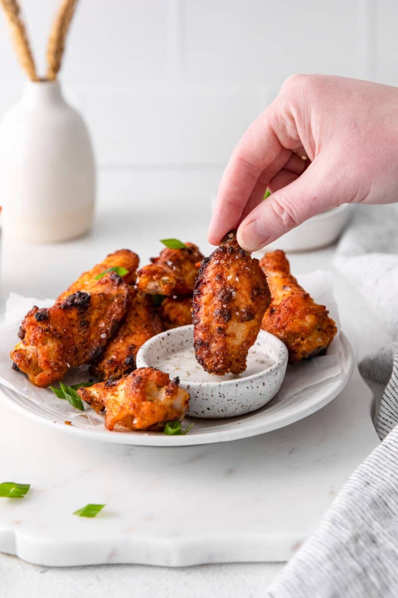 hand dipping a dry rub chicken wing into dipping sauce.