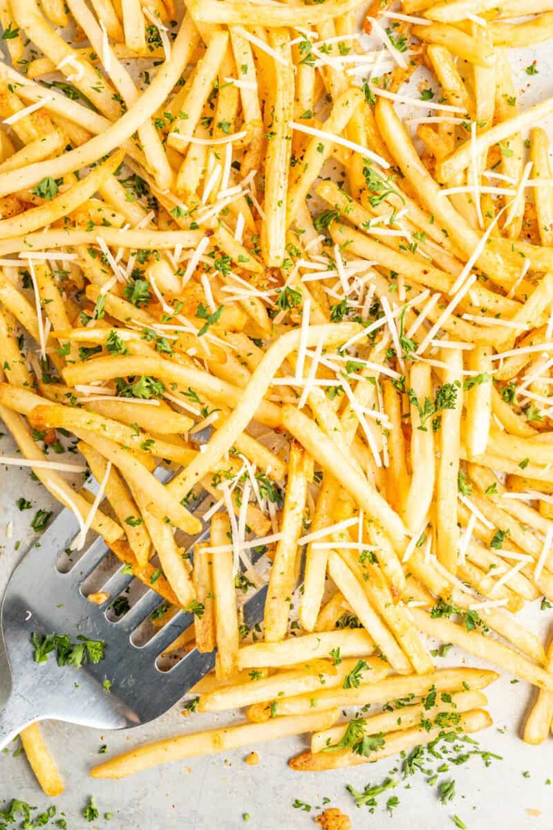 garlic parmesan fries on a sheet pan with a spatula.