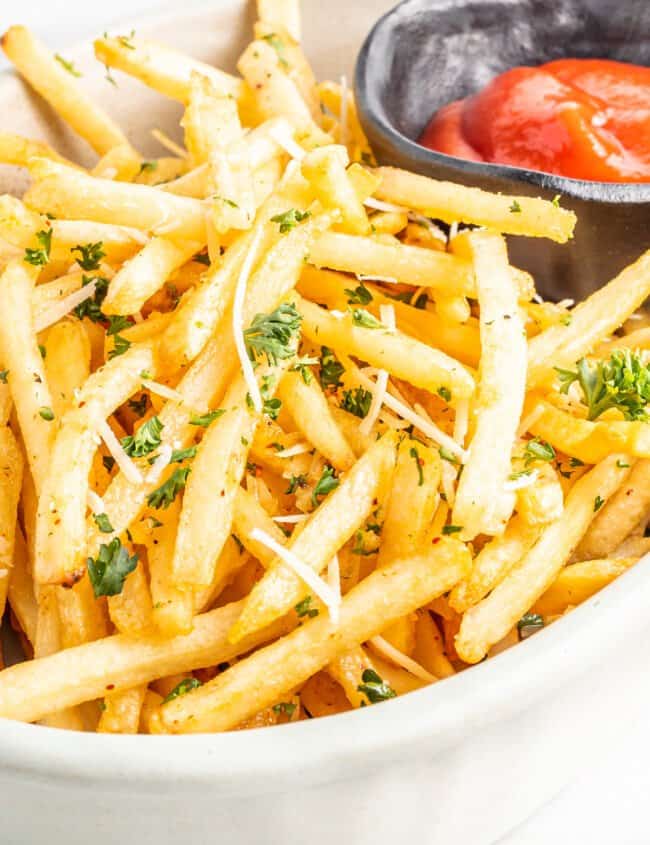 garlic parmesan fries in a white bowl with ketchup.